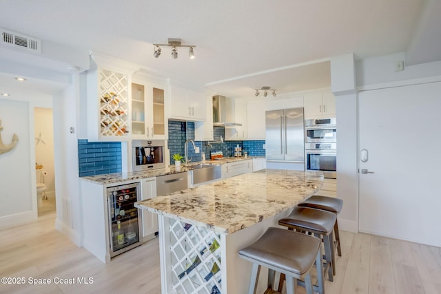 kitchen featuring a sink, tasteful backsplash, stainless steel appliances, wine cooler, and wall chimney range hood