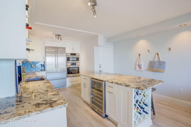 kitchen with light wood finished floors, beverage cooler, decorative backsplash, appliances with stainless steel finishes, and a sink