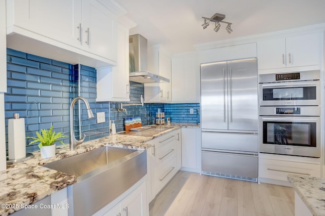 kitchen with a sink, wall chimney range hood, white cabinetry, and stainless steel appliances