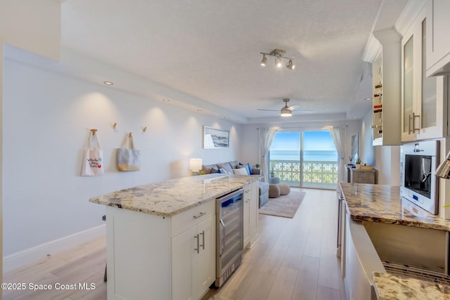 kitchen with beverage cooler, light stone countertops, light wood-style flooring, ceiling fan, and open floor plan