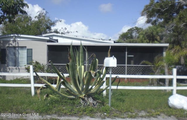 view of front of house featuring stucco siding, fence, and a sunroom