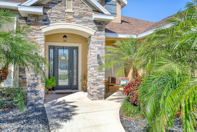 view of exterior entry featuring a shingled roof, stone siding, and stucco siding