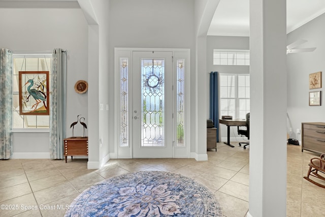 tiled entryway with ceiling fan, baseboards, arched walkways, and a towering ceiling