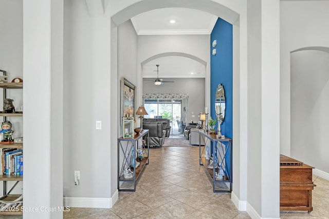 entrance foyer featuring a ceiling fan, arched walkways, crown molding, light tile patterned floors, and baseboards