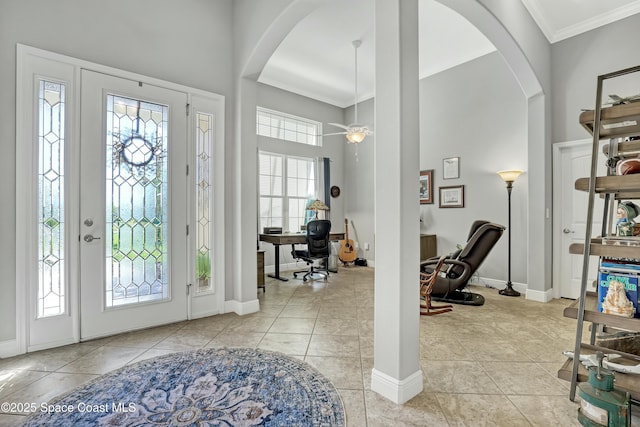 foyer with light tile patterned floors, baseboards, a high ceiling, arched walkways, and crown molding