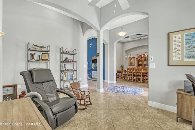 sitting room featuring tile patterned floors, ornamental molding, ceiling fan with notable chandelier, arched walkways, and baseboards