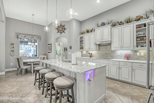 kitchen with light tile patterned floors, arched walkways, under cabinet range hood, black electric cooktop, and tasteful backsplash