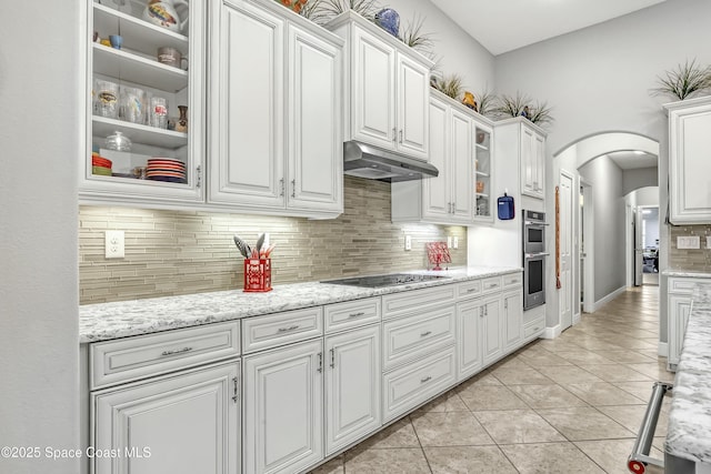 kitchen featuring arched walkways, under cabinet range hood, white cabinetry, double oven, and black electric stovetop