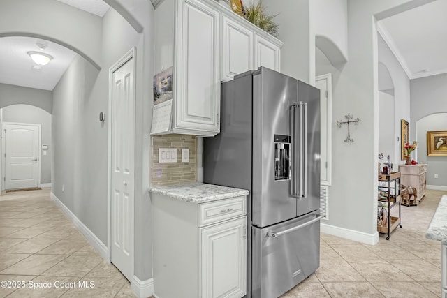 kitchen with baseboards, light tile patterned flooring, high end fridge, white cabinets, and backsplash