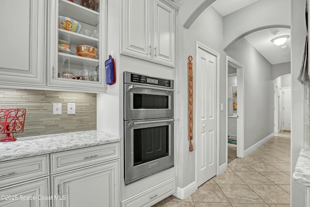 kitchen with backsplash, white cabinetry, arched walkways, double oven, and light tile patterned floors