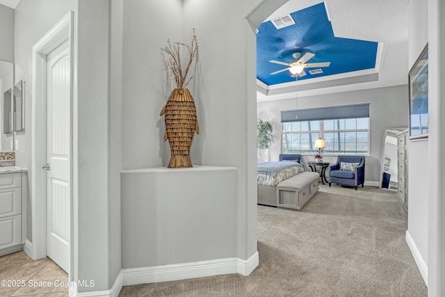 corridor featuring baseboards, a tray ceiling, carpet floors, and visible vents