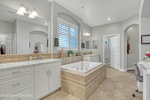 bathroom featuring vanity, a relaxing tiled tub, and visible vents