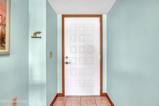 doorway featuring baseboards, a textured ceiling, and light tile patterned flooring