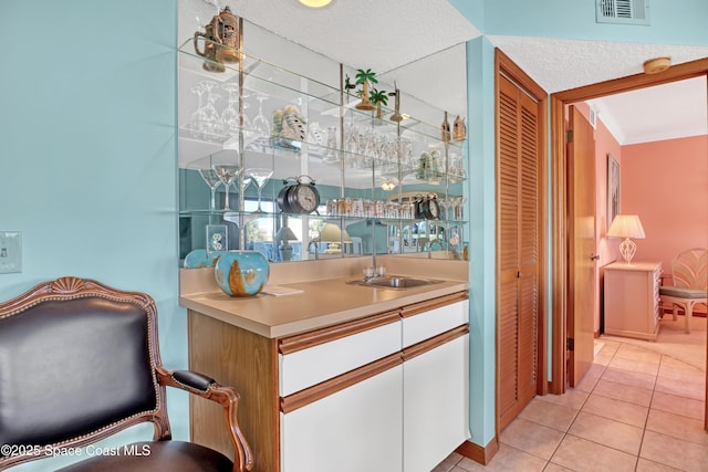 bar featuring visible vents, a sink, crown molding, light tile patterned floors, and indoor wet bar