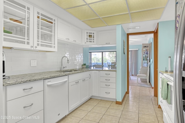 kitchen featuring tasteful backsplash, visible vents, light tile patterned floors, white dishwasher, and a sink