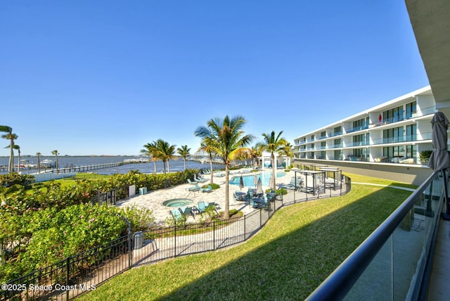 view of home's community with a swimming pool, fence, a water view, and a lawn