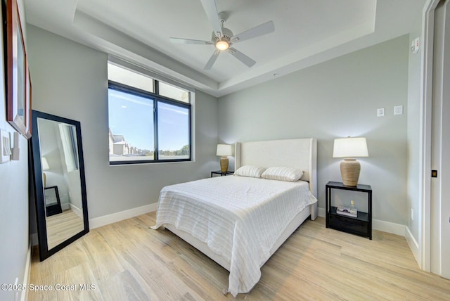 bedroom with a tray ceiling, baseboards, light wood-style floors, and ceiling fan