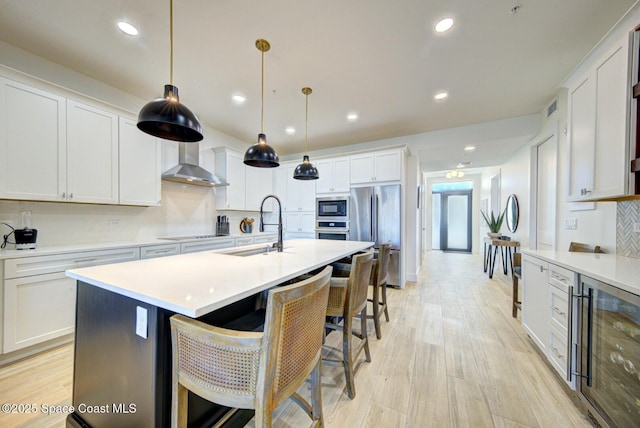 kitchen featuring a sink, wine cooler, appliances with stainless steel finishes, wall chimney exhaust hood, and light countertops