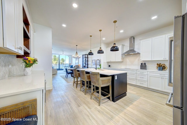 kitchen with decorative backsplash, light countertops, light wood-style floors, white cabinetry, and wall chimney exhaust hood