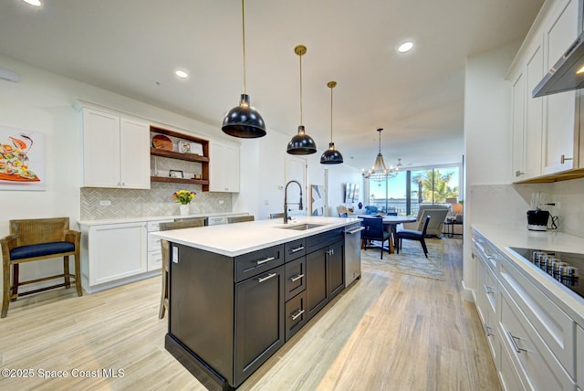 kitchen with light wood-type flooring, light countertops, white cabinetry, wall chimney exhaust hood, and a sink