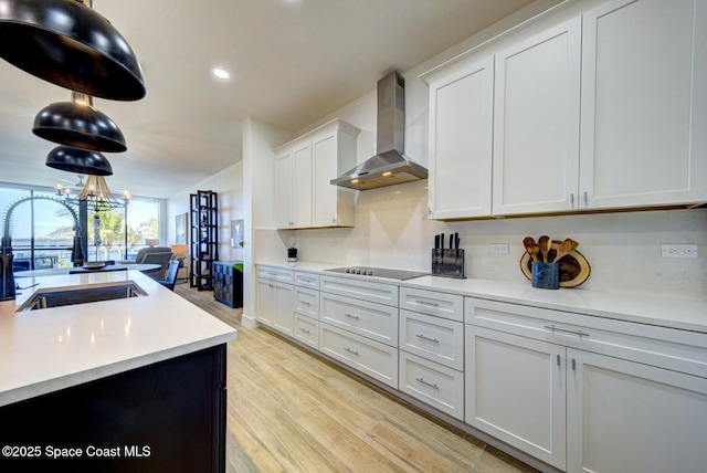 kitchen with light wood-type flooring, light countertops, wall chimney exhaust hood, black electric cooktop, and a sink