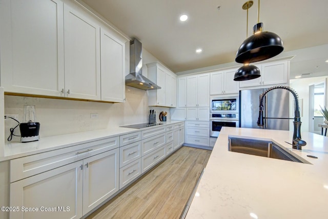 kitchen featuring a sink, stainless steel appliances, light countertops, and wall chimney range hood