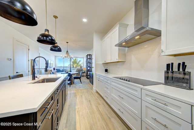 kitchen with black electric cooktop, light countertops, wall chimney range hood, and a sink