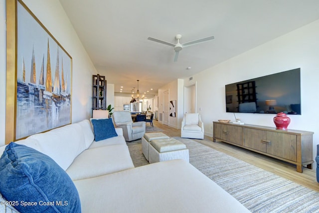 living room featuring baseboards, ceiling fan with notable chandelier, and light wood finished floors