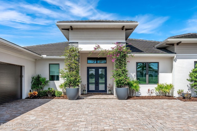 property entrance featuring stucco siding, french doors, a garage, a tile roof, and decorative driveway