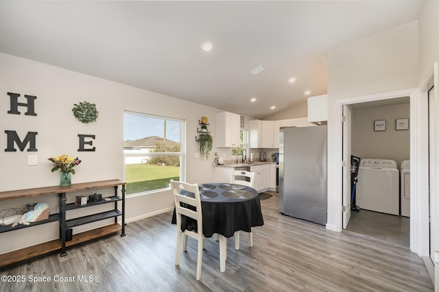 kitchen with lofted ceiling, white cabinets, freestanding refrigerator, washer and dryer, and a sink