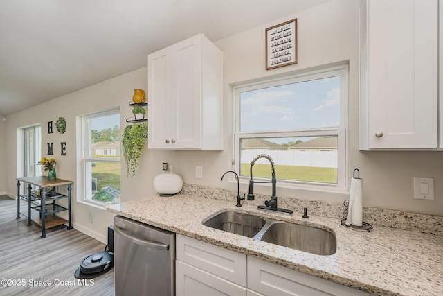 kitchen featuring light wood-style flooring, a sink, light stone counters, stainless steel dishwasher, and white cabinets