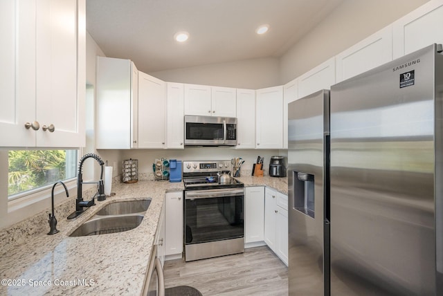 kitchen with a sink, appliances with stainless steel finishes, white cabinets, and vaulted ceiling