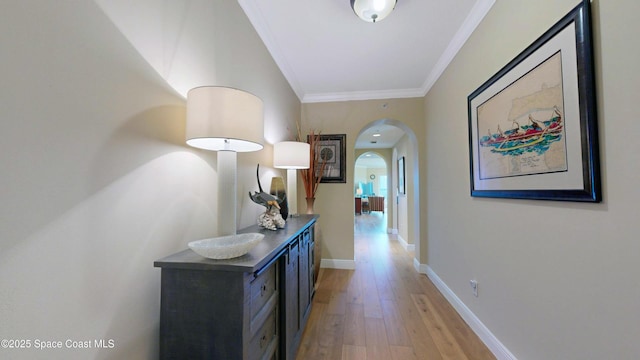 hallway with baseboards, light wood-style floors, arched walkways, and ornamental molding