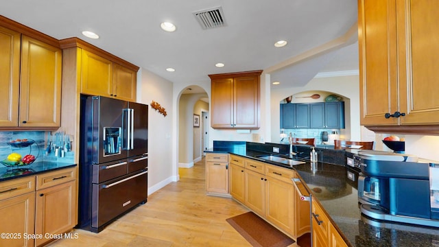 kitchen with visible vents, light wood-style flooring, black fridge, a sink, and arched walkways