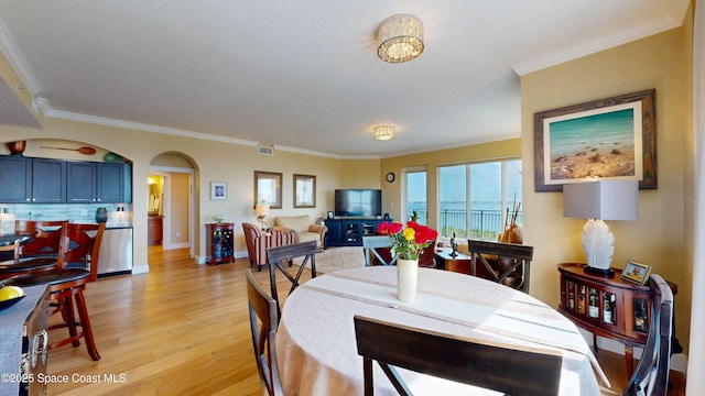 dining area with baseboards, visible vents, arched walkways, ornamental molding, and light wood-type flooring