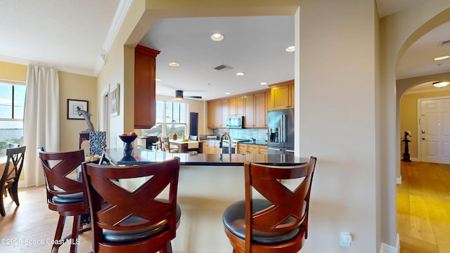 kitchen with visible vents, a breakfast bar, light wood-style flooring, tasteful backsplash, and stainless steel appliances