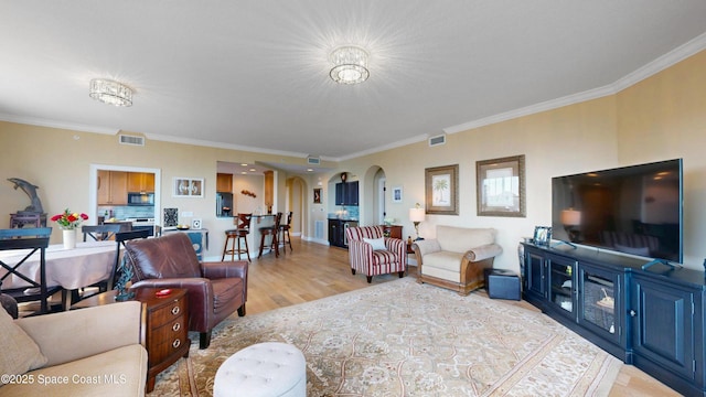 living room with arched walkways, visible vents, light wood-style floors, and ornamental molding