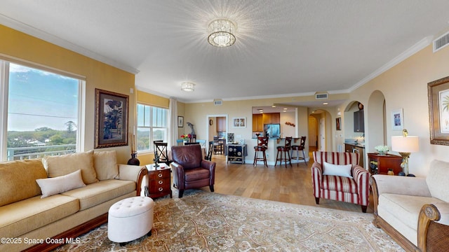 living area featuring ornamental molding, wood finished floors, visible vents, and arched walkways