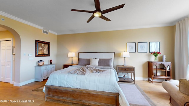 bedroom with visible vents, arched walkways, crown molding, light wood finished floors, and baseboards