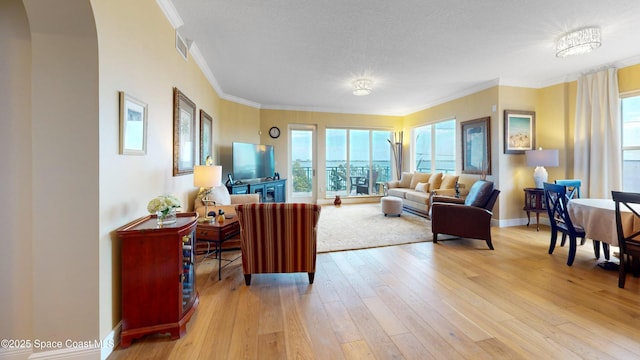 living area featuring visible vents, baseboards, arched walkways, ornamental molding, and light wood-style floors