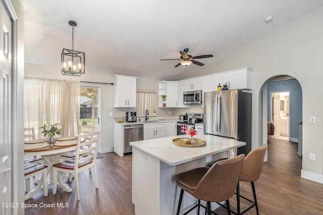 kitchen with arched walkways, a sink, appliances with stainless steel finishes, white cabinetry, and ceiling fan with notable chandelier