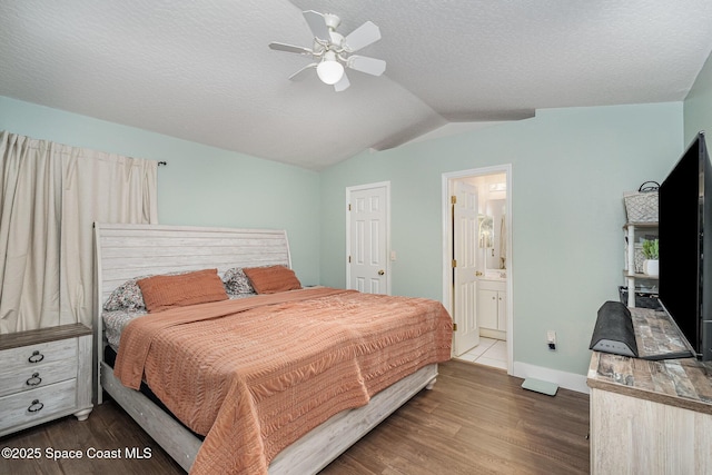 bedroom featuring a textured ceiling, ensuite bath, dark wood-style floors, baseboards, and vaulted ceiling