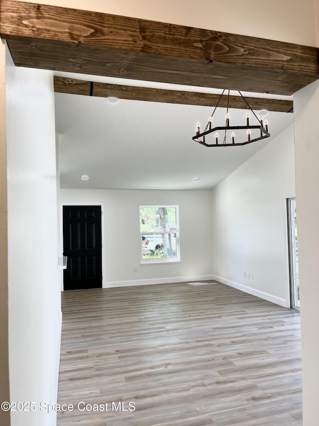 unfurnished room featuring beam ceiling, baseboards, light wood finished floors, and a chandelier