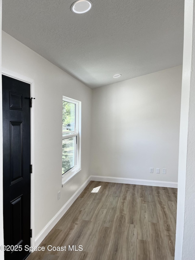 spare room featuring baseboards, a textured ceiling, and wood finished floors