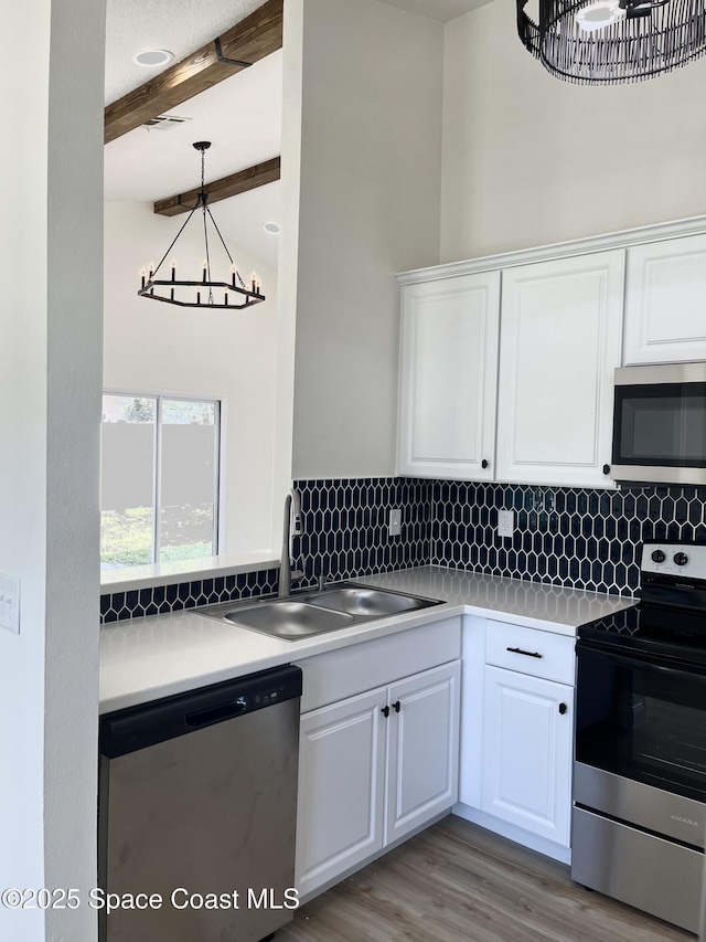 kitchen featuring beamed ceiling, a sink, tasteful backsplash, white cabinetry, and appliances with stainless steel finishes