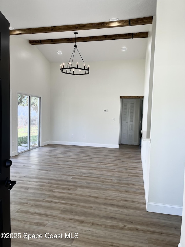 spare room with baseboards, light wood-type flooring, beam ceiling, a high ceiling, and a notable chandelier