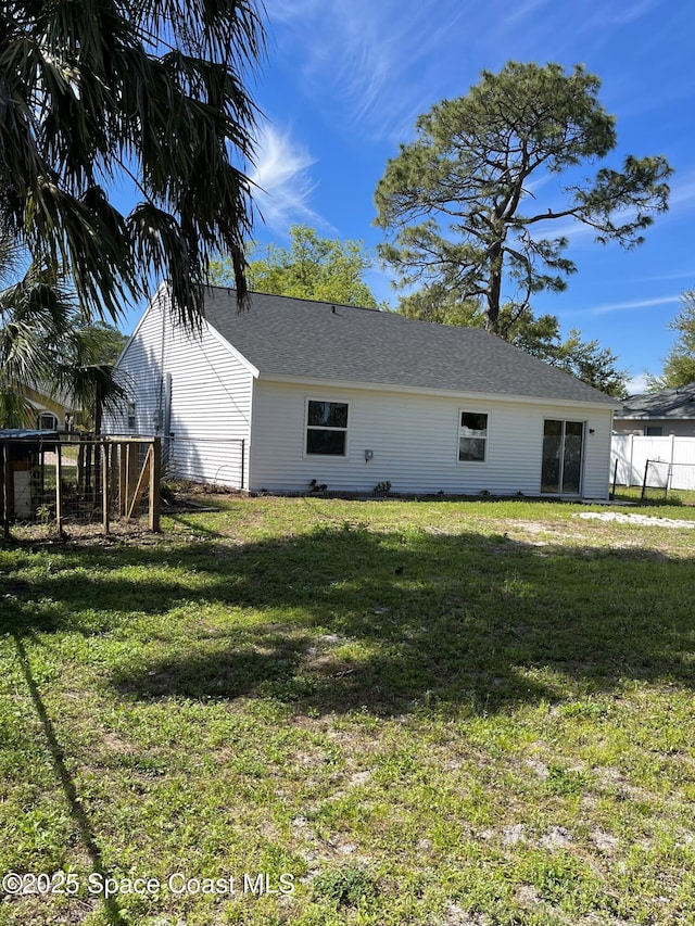 back of property featuring a lawn, roof with shingles, and fence