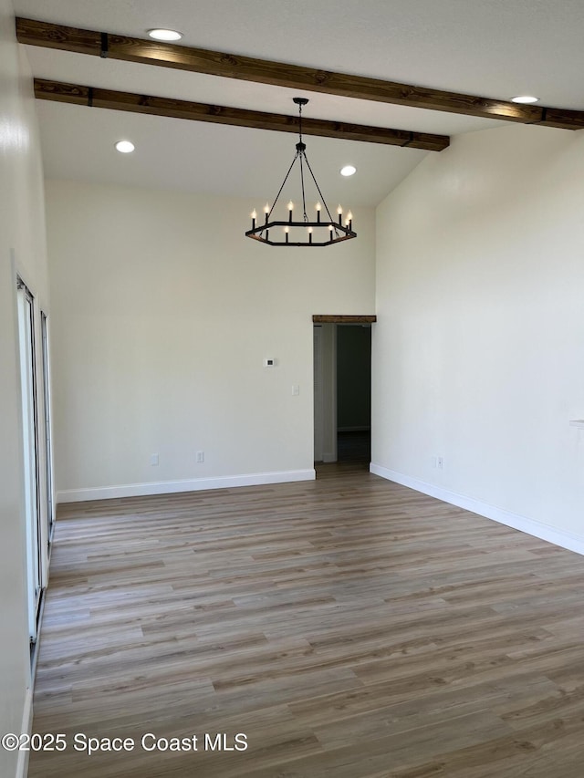 empty room featuring baseboards, an inviting chandelier, wood finished floors, and vaulted ceiling with beams