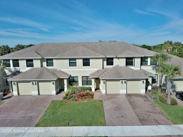 townhome / multi-family property with stucco siding, driveway, a front yard, and a garage