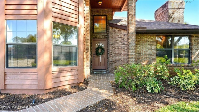 view of exterior entry with brick siding and a chimney